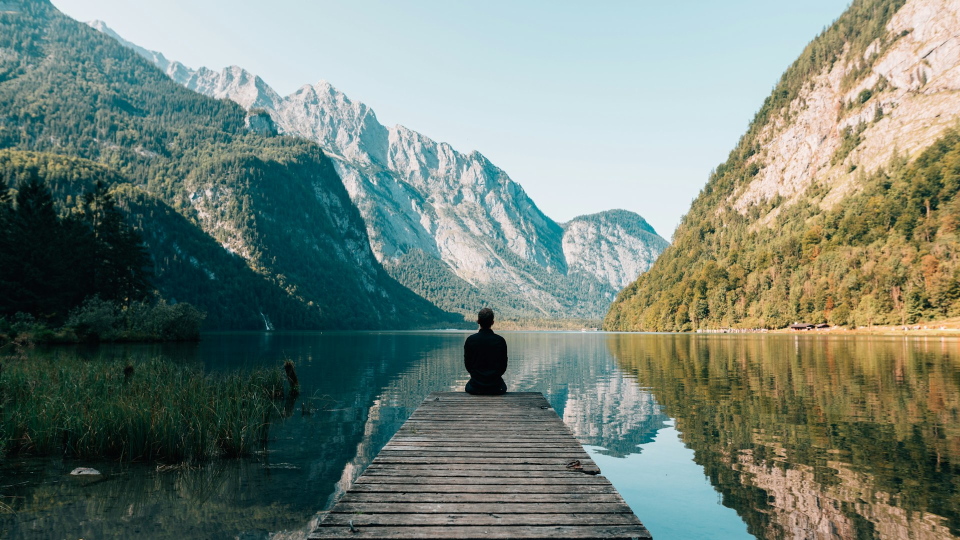 Persona sentada en calma frente a un lago rodeado de montañas verdes