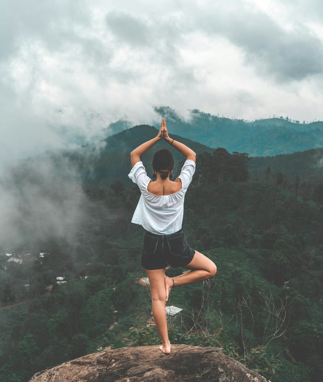 Persona practicando yoga en calma sobre una montaña entre naturaleza verde